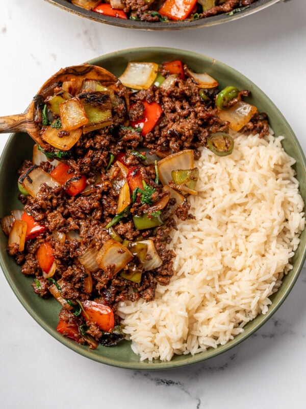 adding Thai basil beef stir fry to a bowl of rice with a wooden spoon