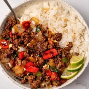 Thai basil beef stir fry in a bowl with coconut rice and lime wedges