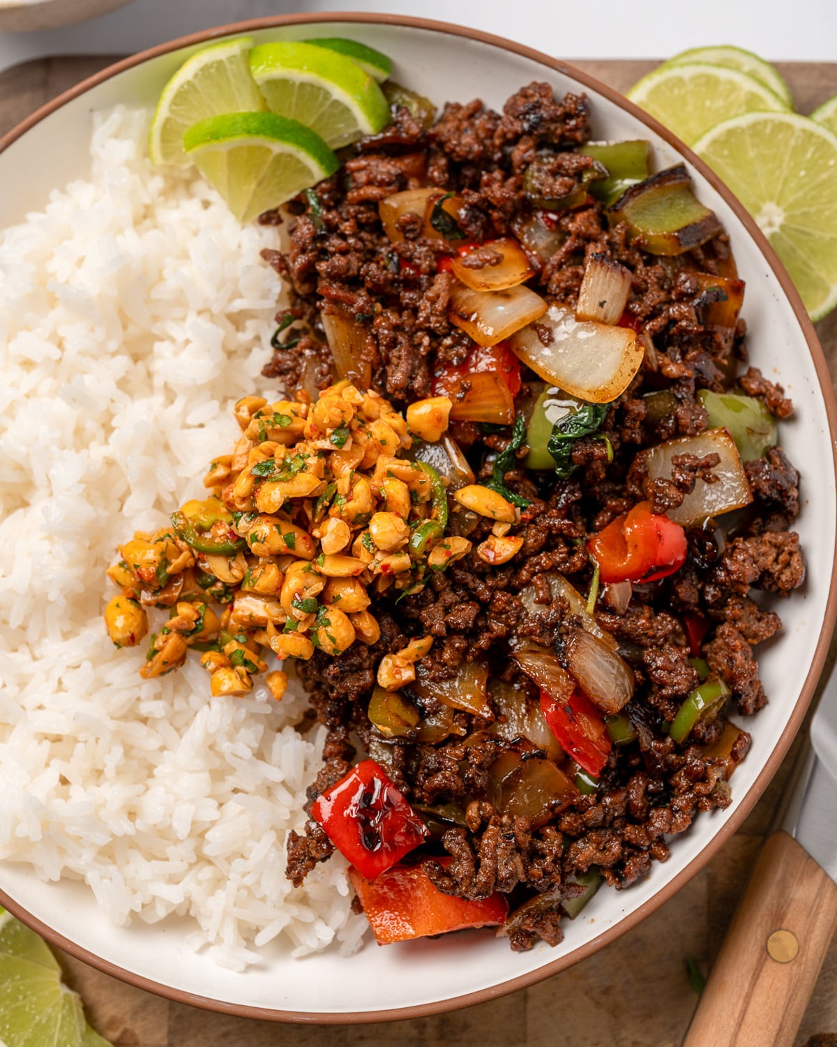 Thai basil beef and rice bowl with chopped peanut garnish and lime wedges