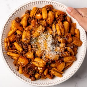 picking up a bowl of ground beef and bell pepper pasta garnished with parmesan, black pepper, and olive oil