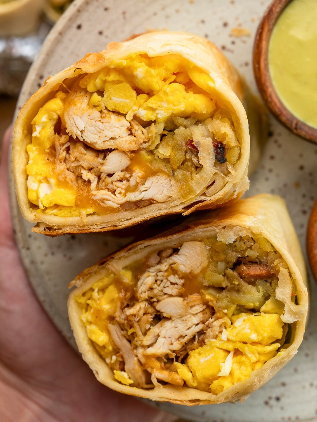 a halved chicken breakfast burrito on a plate with hot sauce