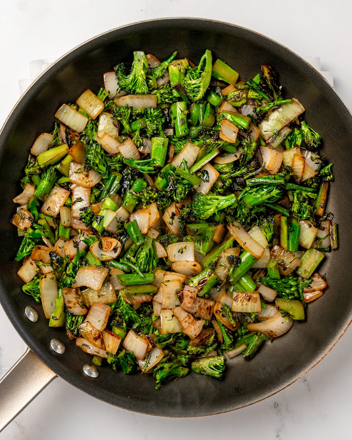 stir fried broccolini and onion in a nonstick pan