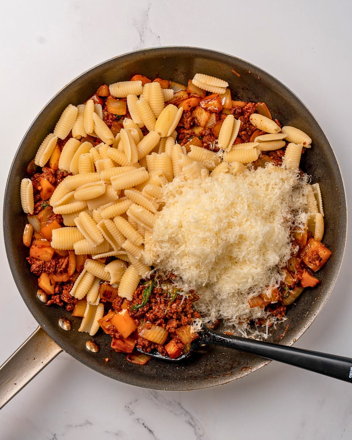 cooked pasta and grated parmesan cheese in a pan with cooked ground beef and bell peppers