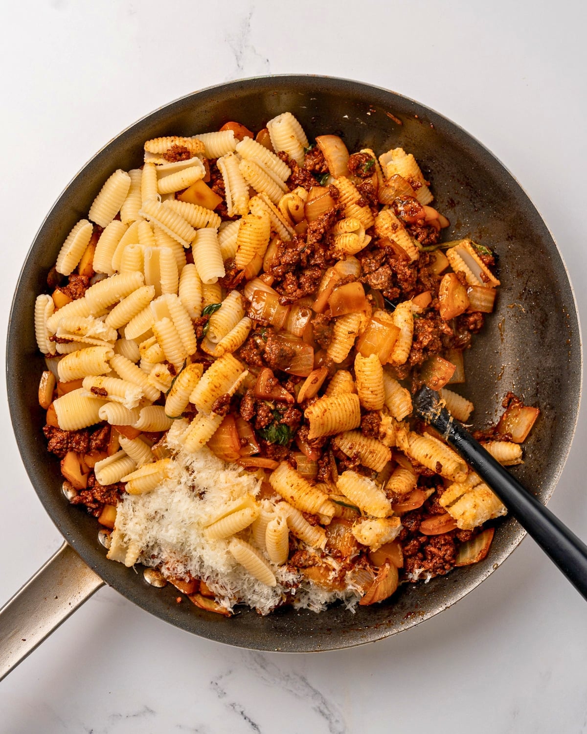 stirring a pan of bell pepper and beef pasta with a rubber spatula