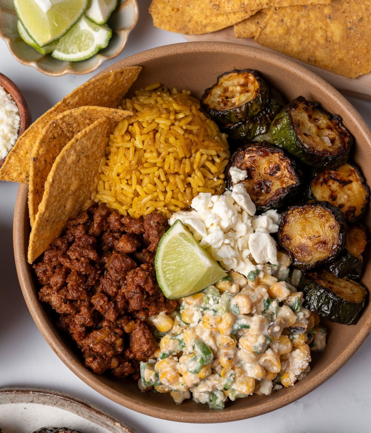 roasted zucchini in a bowl with street corn salad, taco beef, queso fresco, rice, and tortilla chips
