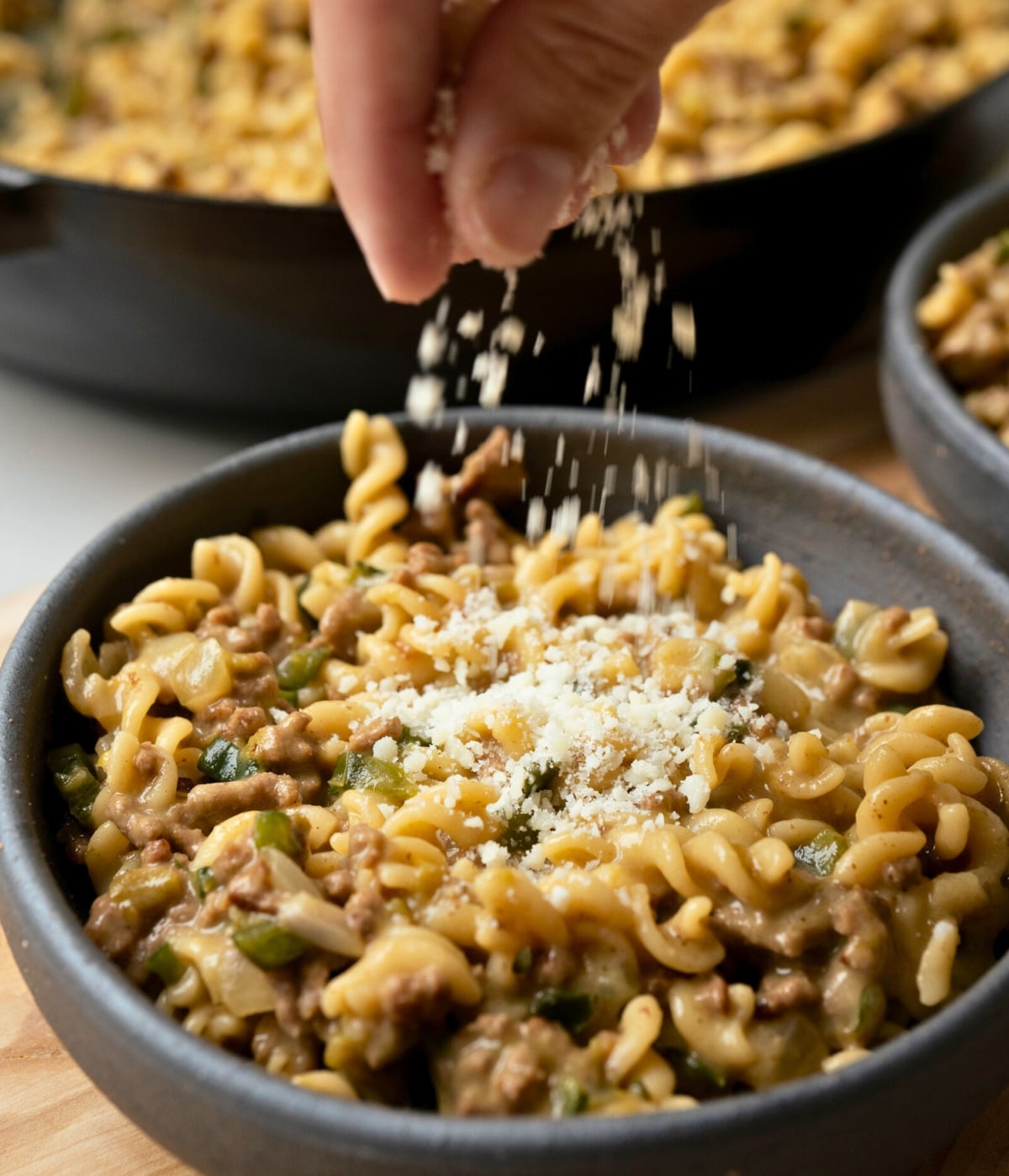 sprinkling cotija cheese over a bowl of green chile beef pasta