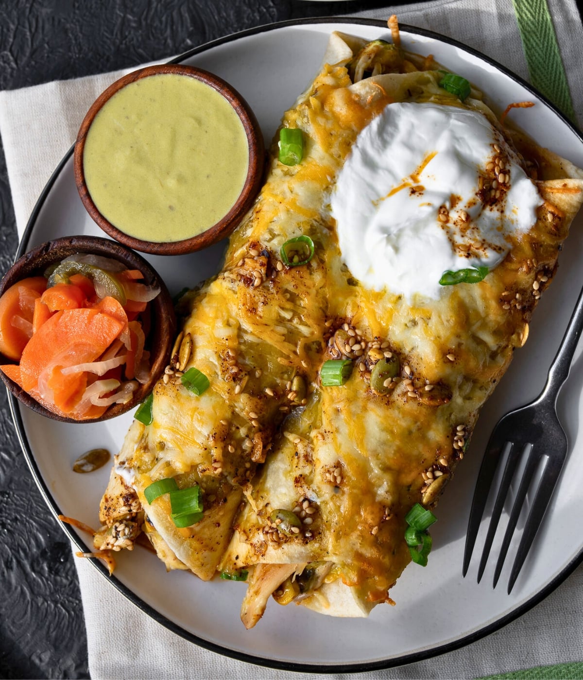 two roasted vegetable enchiladas on a plate with small bowls of escabeche and salsa verde