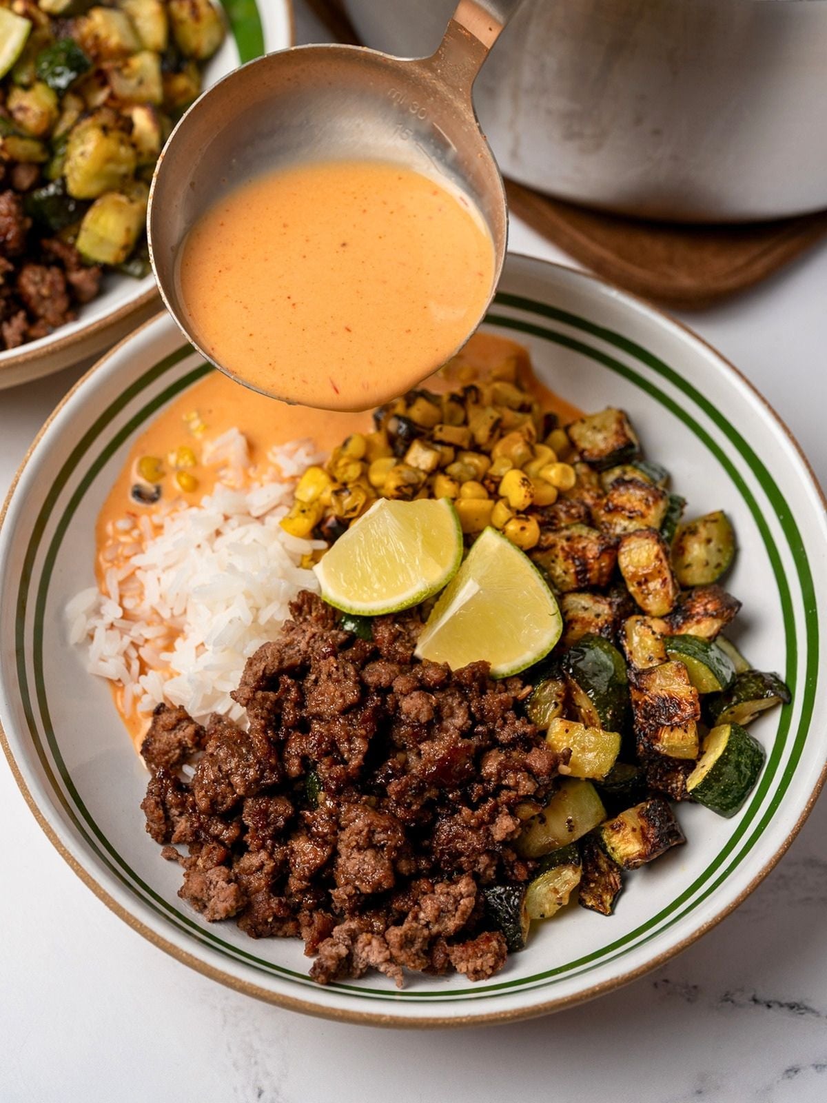 pouring creamy chipotle broth over a bowl of jasmine rice, roasted zucchini and corn, ground beef crumbles, and lime wedges