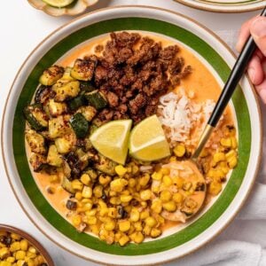eating a bowl of chipotle brothy rice bowl with honey garlic ground beef, roasted zucchini, fire roasted corn, jasmine rice, and lime wedges
