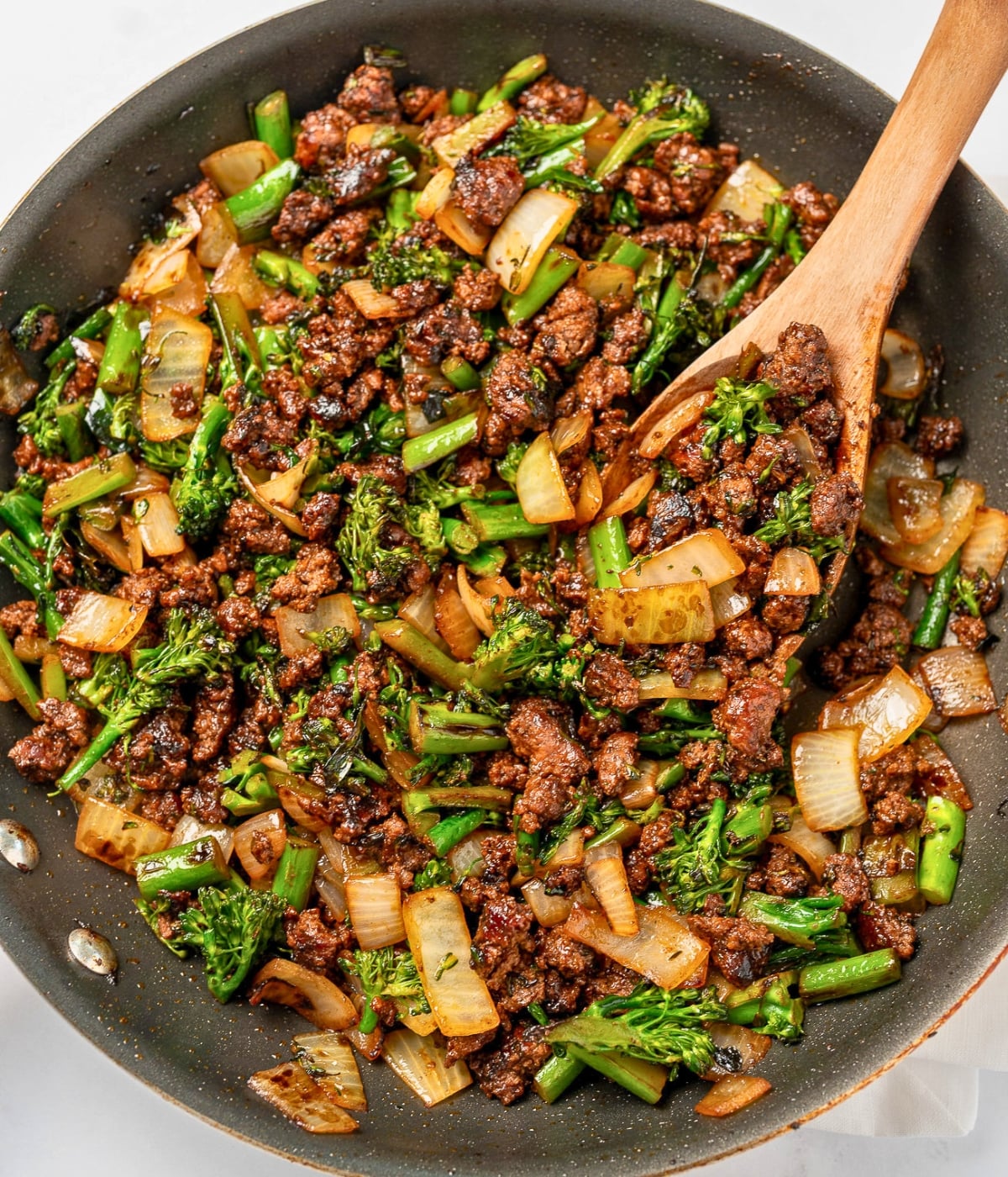 serving a ground beef and baby broccoli from a nonstick pan with a wooden spoon