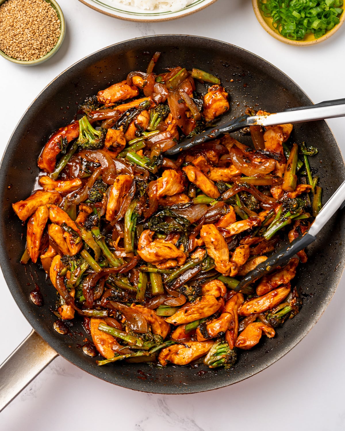 tongs serving chicken stir fry from a nonstick pan
