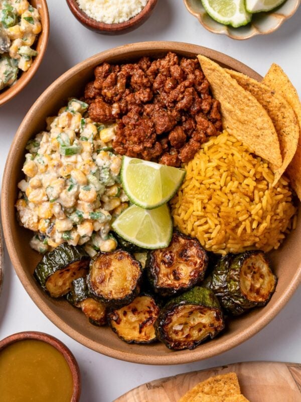 roasted zucchini in a bowl with street corn salad, taco beef, queso fresco, rice, tortilla chips, and lime wedges