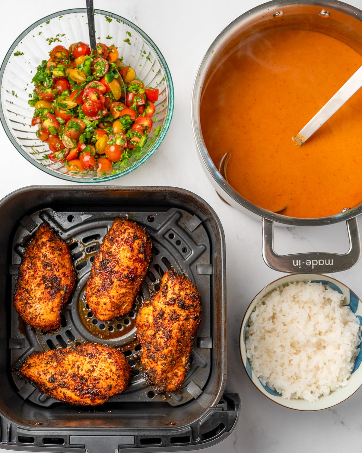 four air fried blackened chicken breasts in an air fryer basket next to a bowl of tomato salsa, pot of tomato cheddar broth, and a bowl of steamed rice