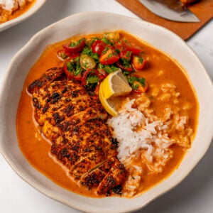 blackened chicken breast in a bowl with steamed rice, lemon wedges, tomatoes, and a cajun broth