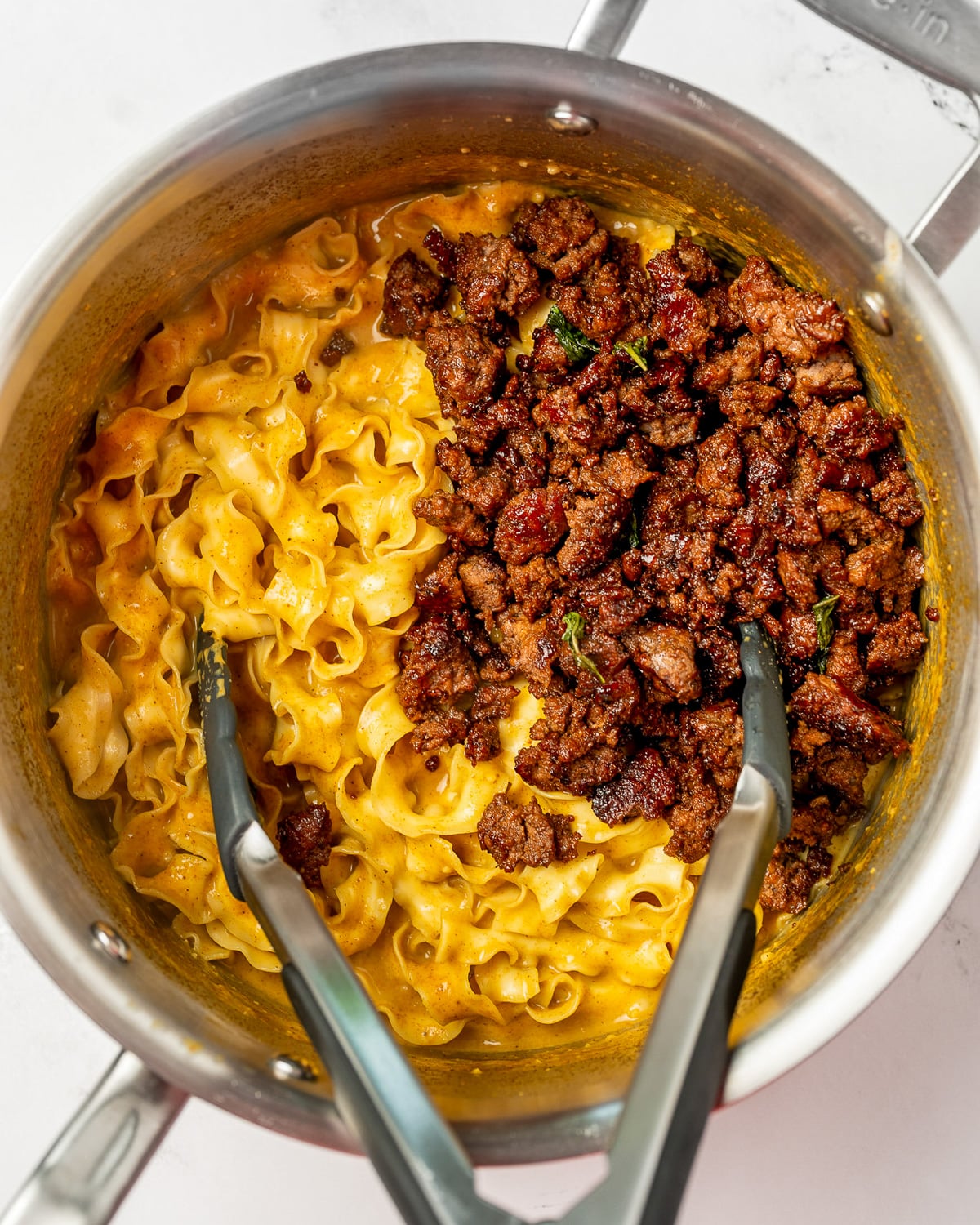 coconut curry noodles and crispy beef crumbles in a saucepan with tongs before mixing