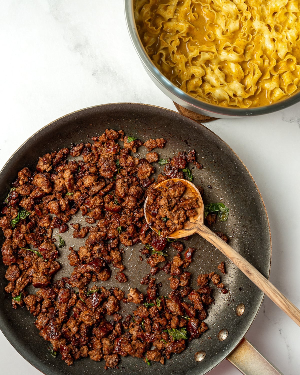 crispy Thai basil ground beef crumbles in a nonstick pan next to a saucepan with coconut curry noodles