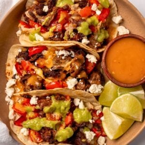 three steak tacos on a plate with habanero hot sauce and lime wedges