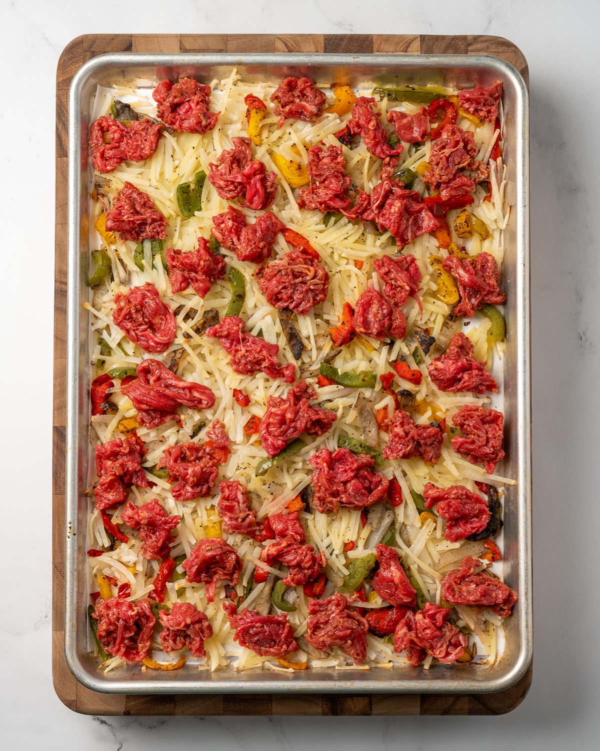 baked hash browns and peppers topped with marinated shaved steak on a sheet pan