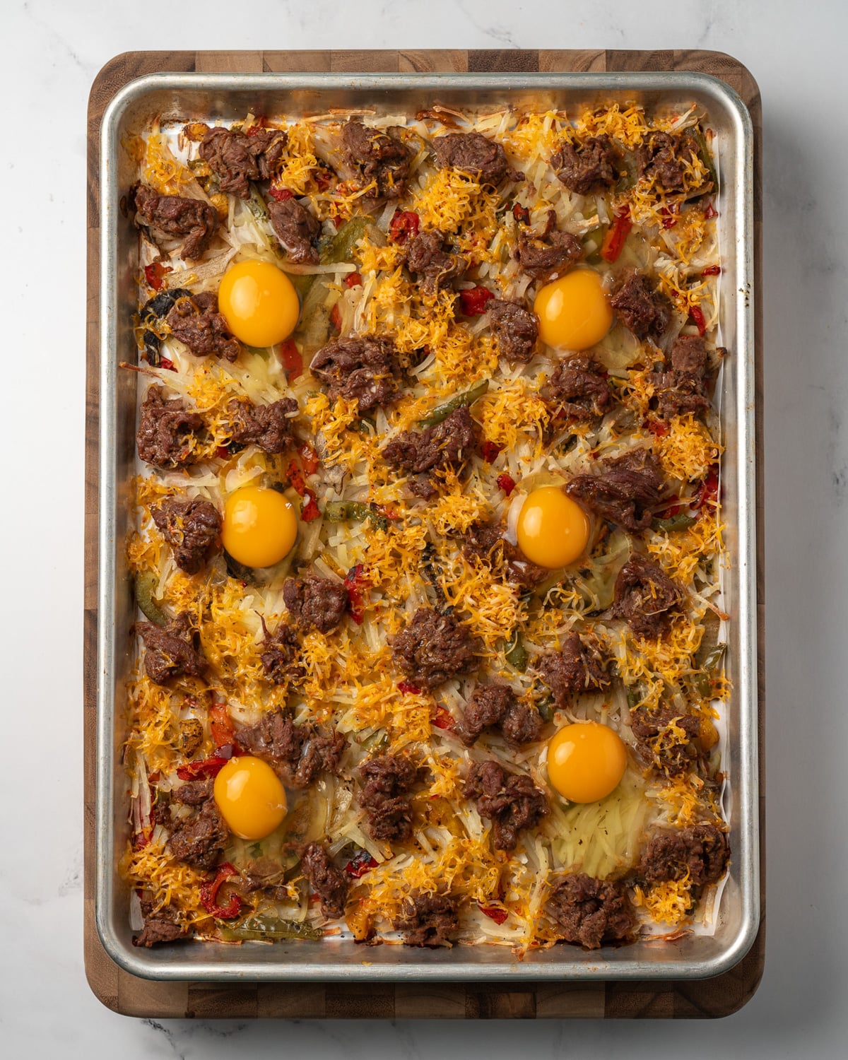 sheet pan baked steak and hash browns topped with 6 eggs and shredded colby jack cheese