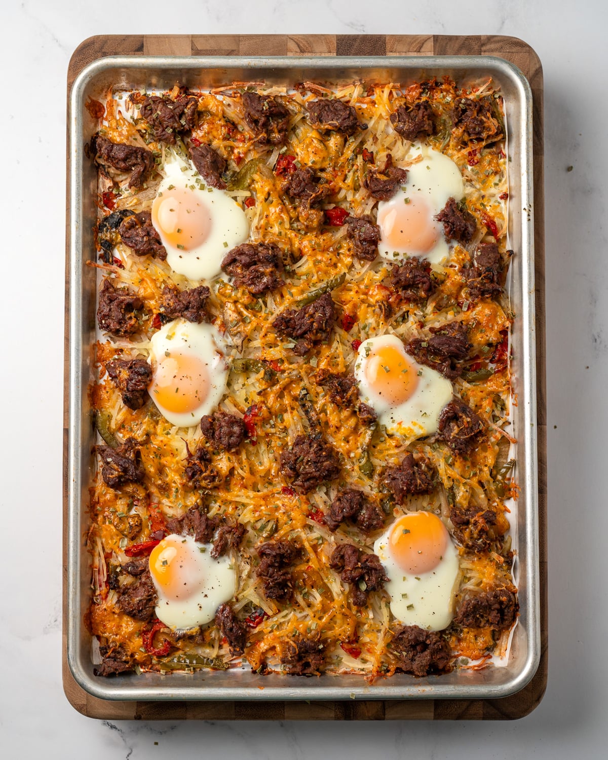 baked steak and eggs with hash browns and peppers on a half sheet pan