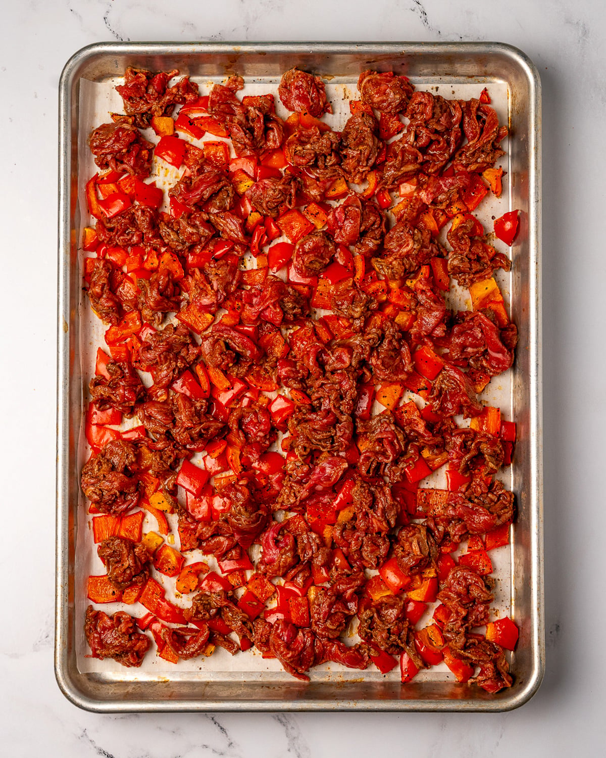 marinated shaved steak on top of roasted peppers on the sheet pan
