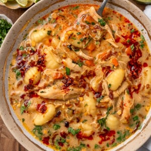 a silver spoon in a bowl of chicken gnocchi soup with chili crisp and Thai basil garnishes