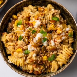 creamy corn and ground chicken pasta in a green bowl garnished with cotija cheese, diced jalapeño pepper, and salsa macha