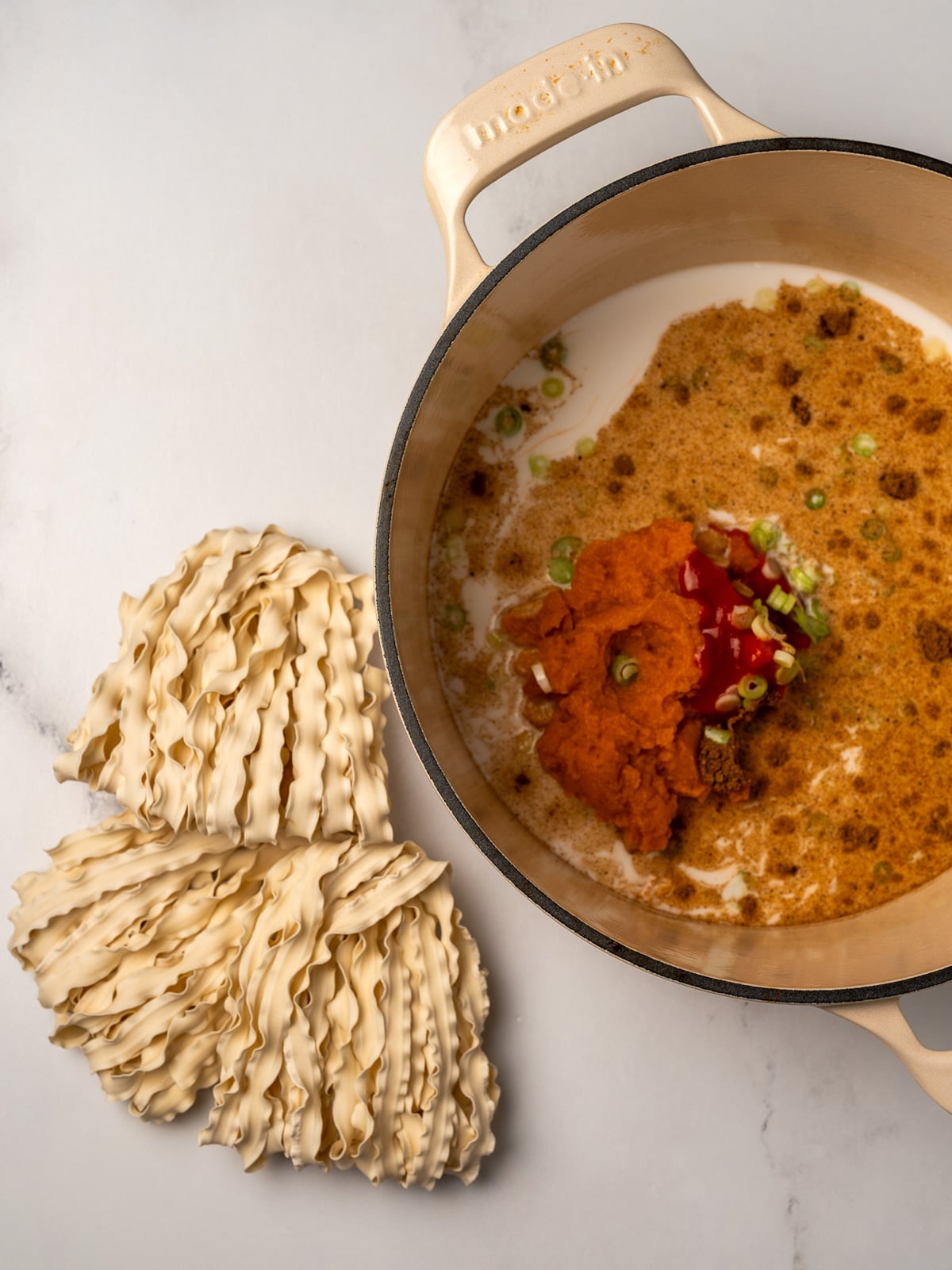 canned pumpkin and coconut milk broth in a Dutch oven next to three blocks of instant wheat noodles