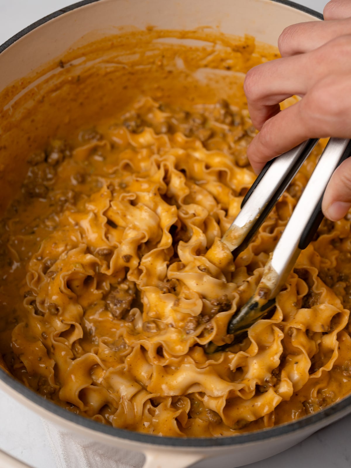 mixing pumpkin noodles and crispy beef together with tongs
