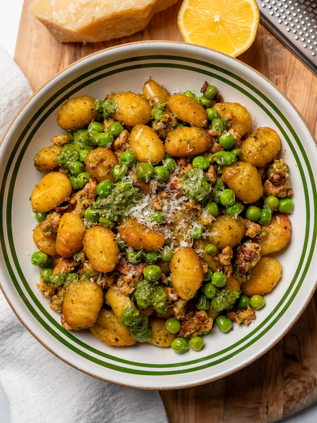 a bowl of crispy gnocchi with sausage and peas on a cutting board with parmesan and a sliced lemon