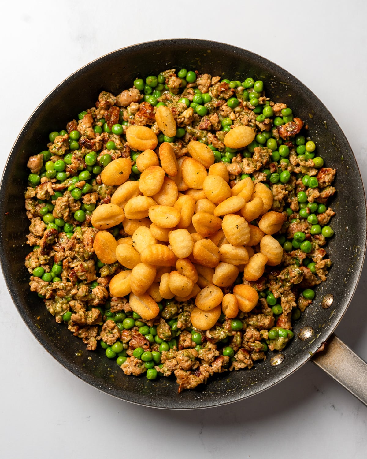 crispy air fried gnocchi on top of a pan with chicken sausage, pea, pesto, and parmesan mixture