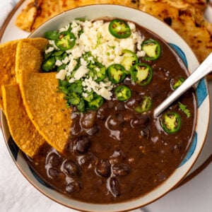 chicken quesadillas next to a bowl of black bean soup in a bowl garnished with tortilla chips, sliced peppers, cotija cheese, and cilantro