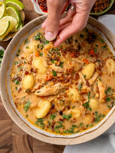 adding crispy shallots to a bowl of curry chicken and gnocchi soup
