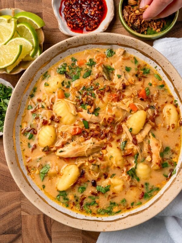 curried chicken and gnocchi soup in a bowl garnished with chili crisp, Thai basil, crispy shallots, and lime wedges