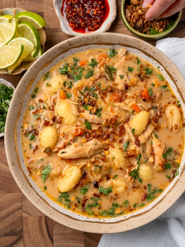 curried chicken and gnocchi soup in a bowl garnished with chili crisp, Thai basil, crispy shallots, and lime wedges