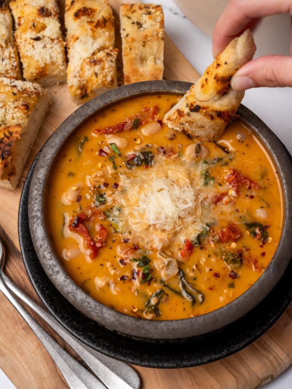 dipping bread in a bowl of marry me chicken soup topped with grated parmesan