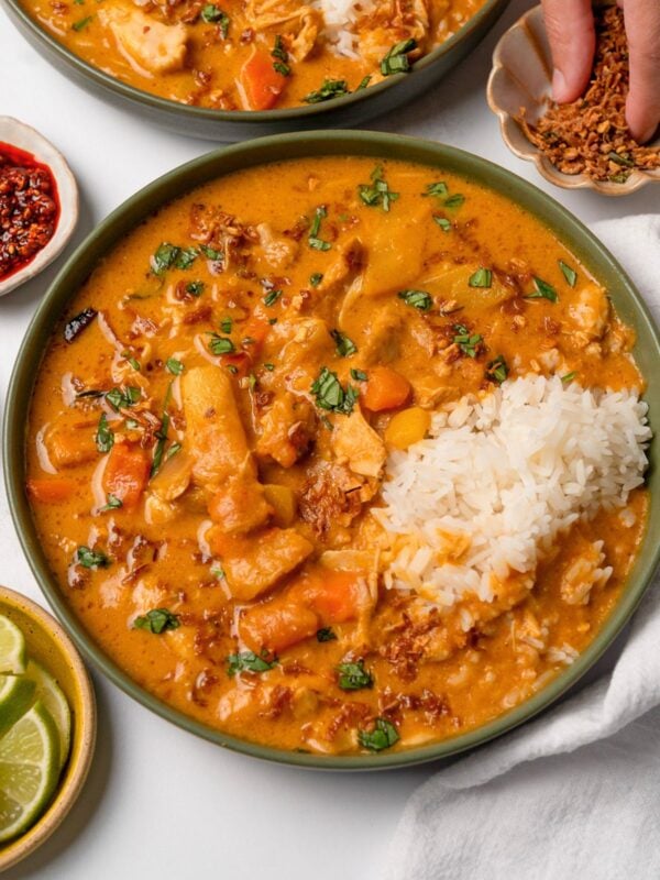 topping a bowl of pumpkin curry and steamed rice with crispy shallots and chopped Thai basil