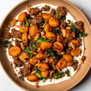 crispy roasted pumpkin gnocchi with kale, maple balsamic ground beef, and whipped goat cheese in a brown bowl