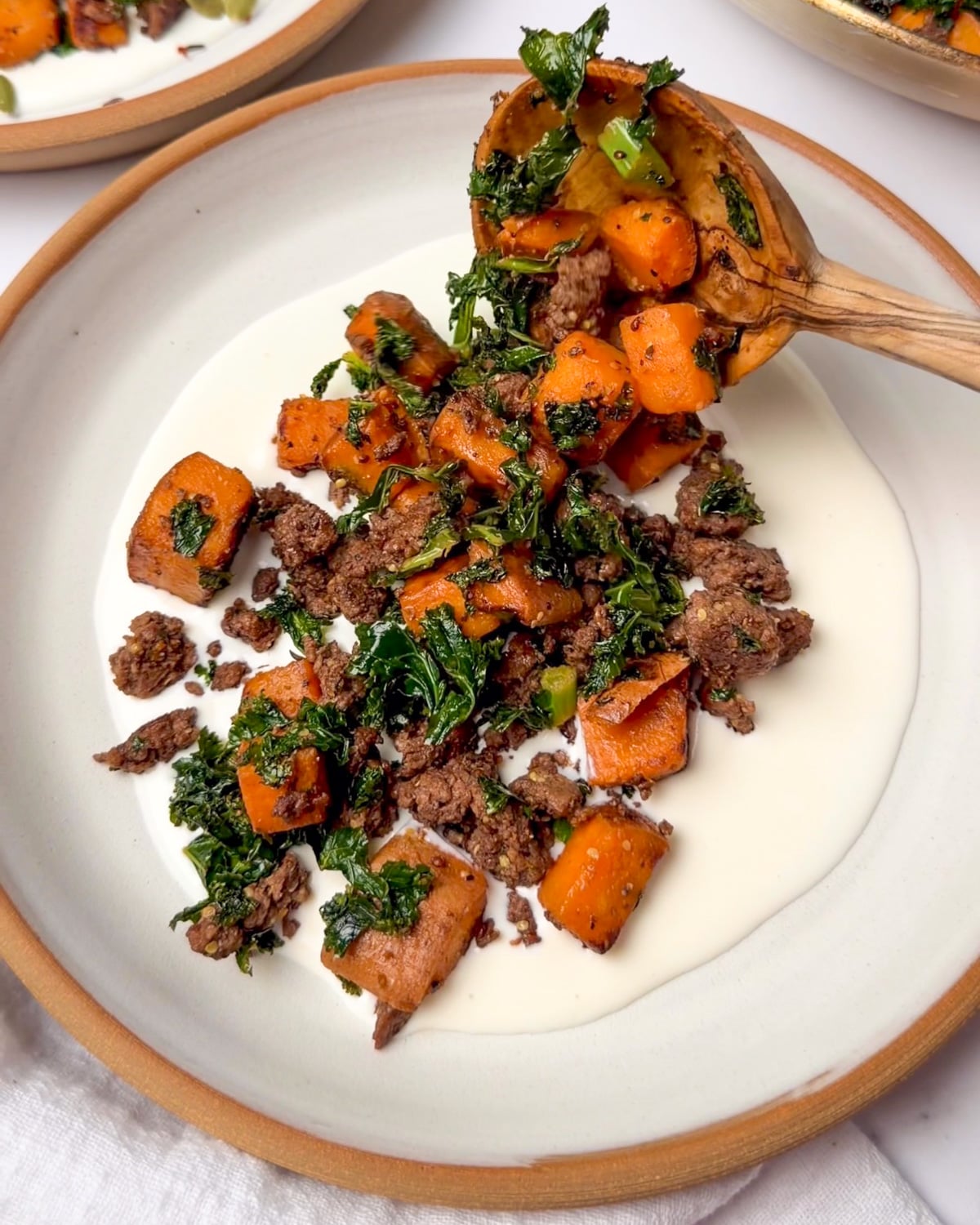 serving sweet potatoes and ground beef over whipped goat cheese with a wooden spoon