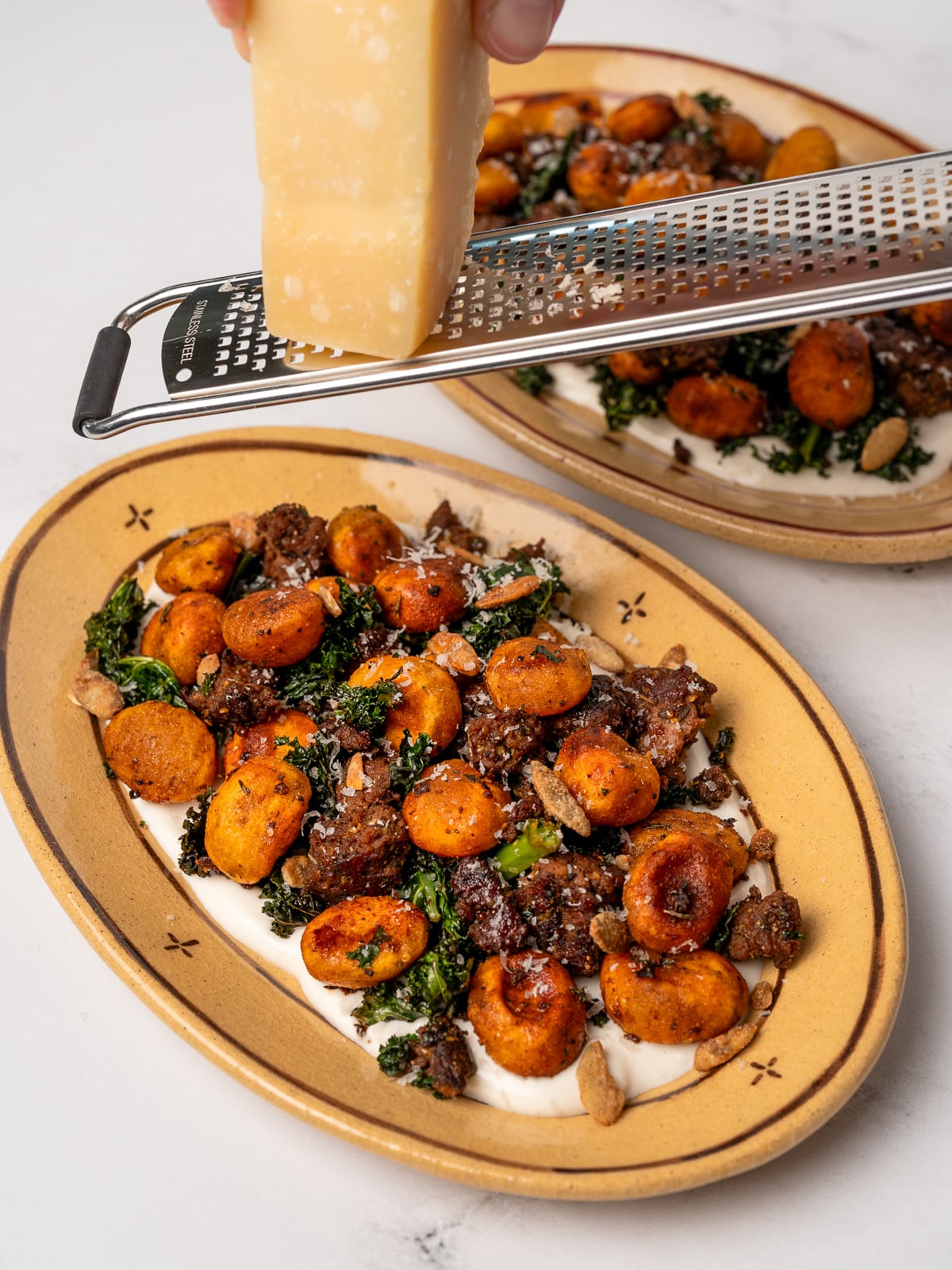 grating parmesan over plates of pumpkin gnocchi and kale