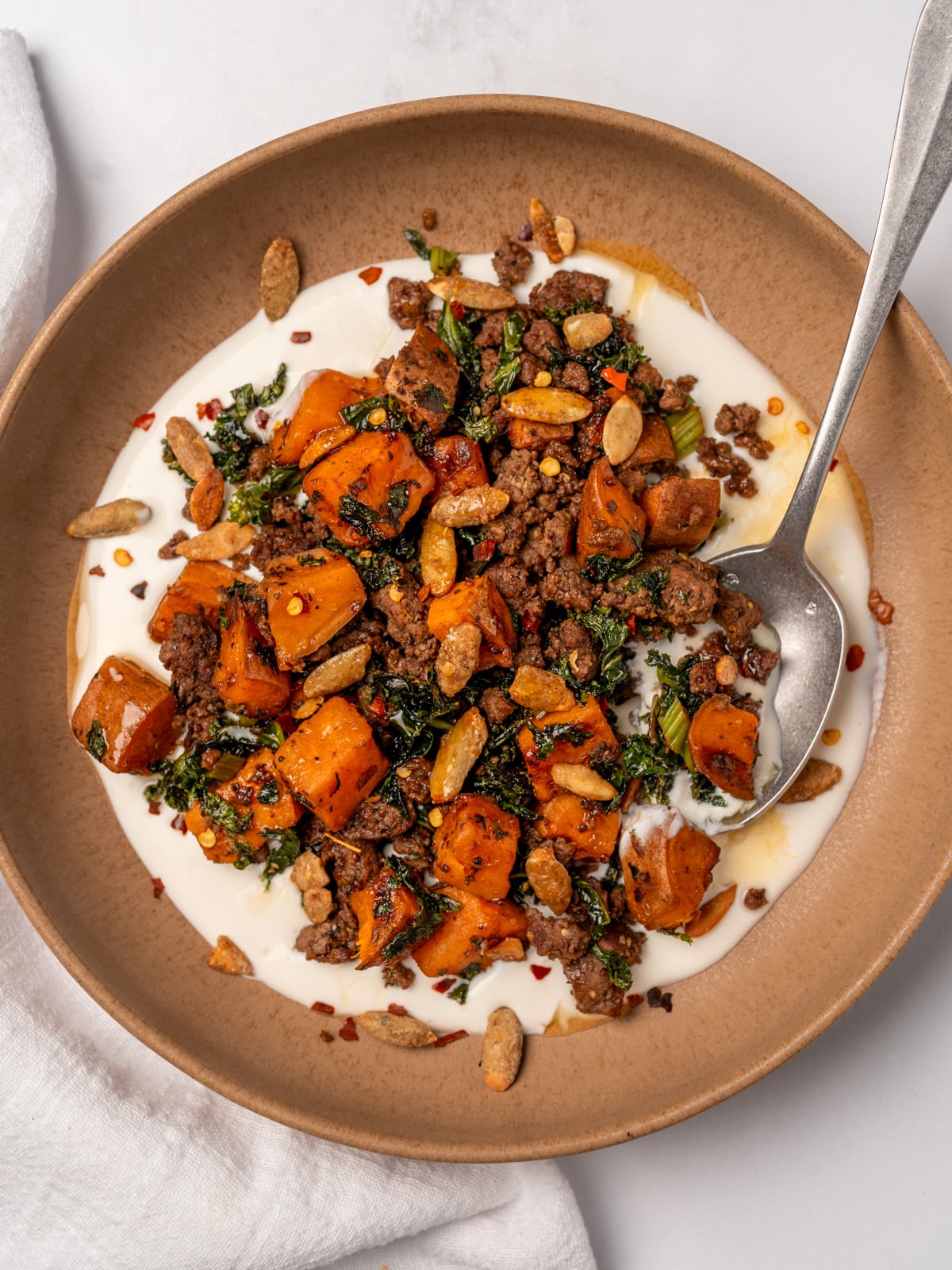 whipped goat cheese smear in a brown bowl topped with ground beef, sweet potatoes and kale, and pumpkin seeds