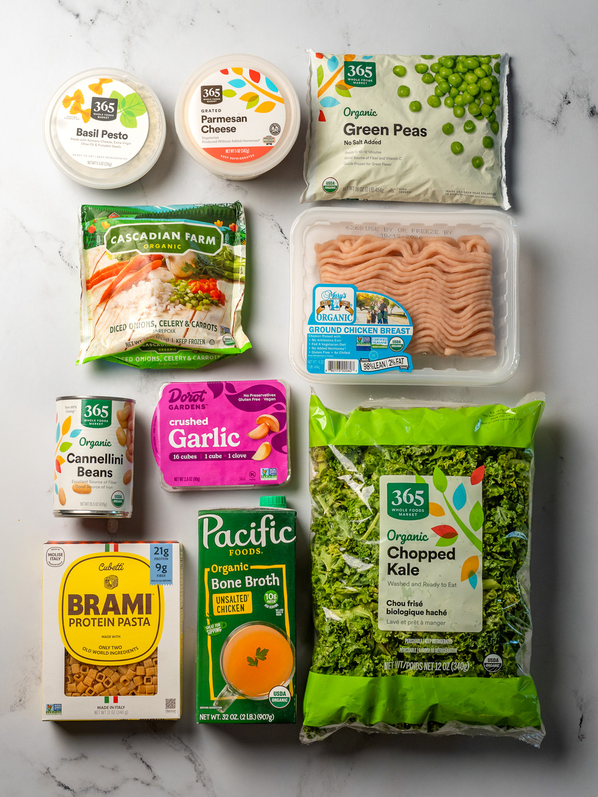 basil pesto, grated parmesan, frozen peas, frozen mirepoix, ground chicken breast, canned cannellini beans, frozen crushed garlic, Brami protein pasta, chicken bone broth, and chopped kale