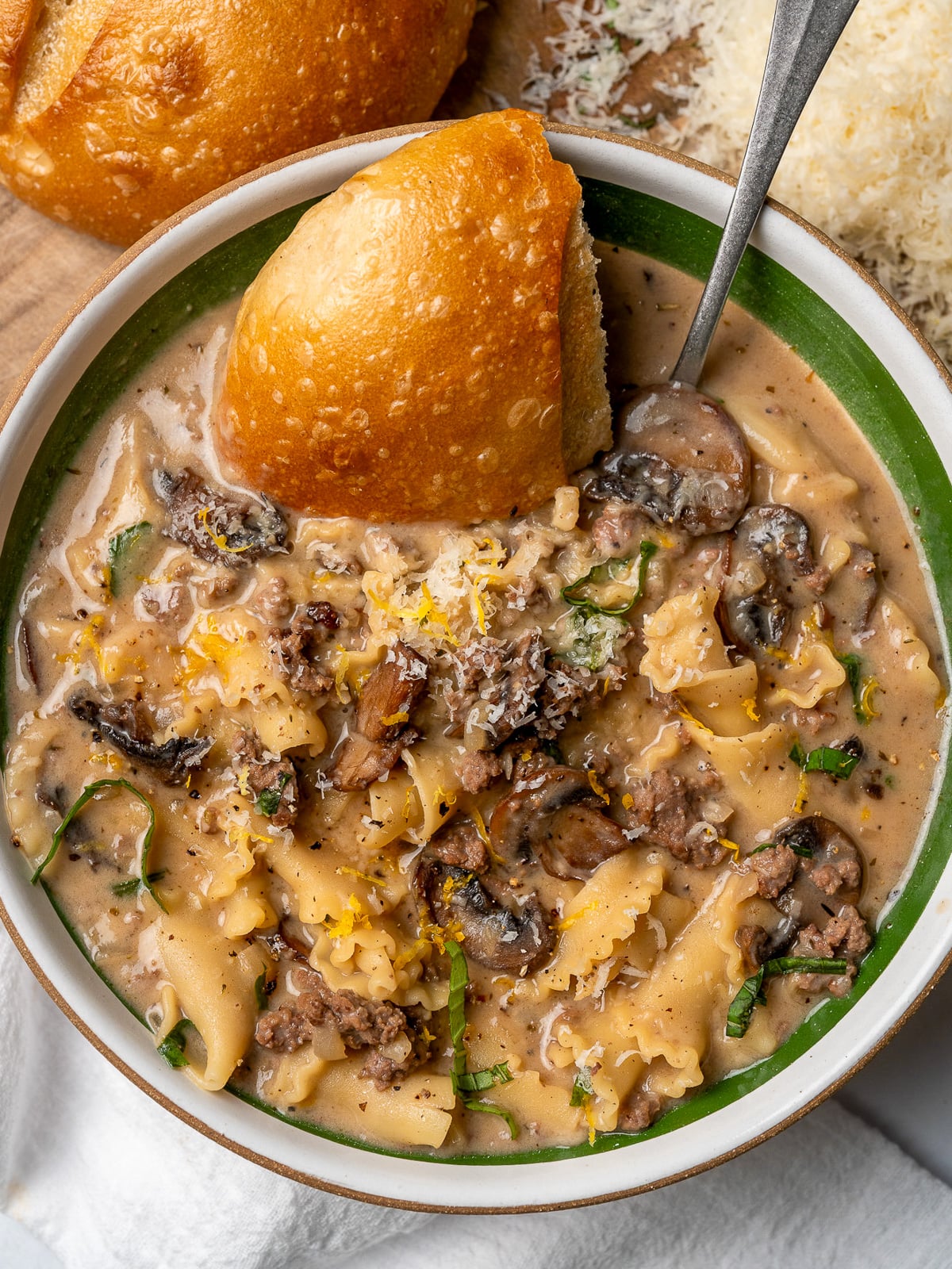 bowl of creamy lasagna soup with sourdough bread, parmesan, lemon zest, and chopped basil