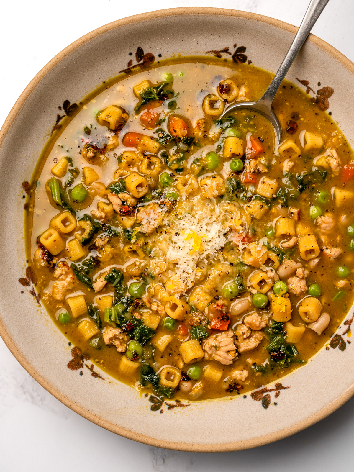 silver spoon in a bowl of chicken minestrone garnished with parmesan and lemon