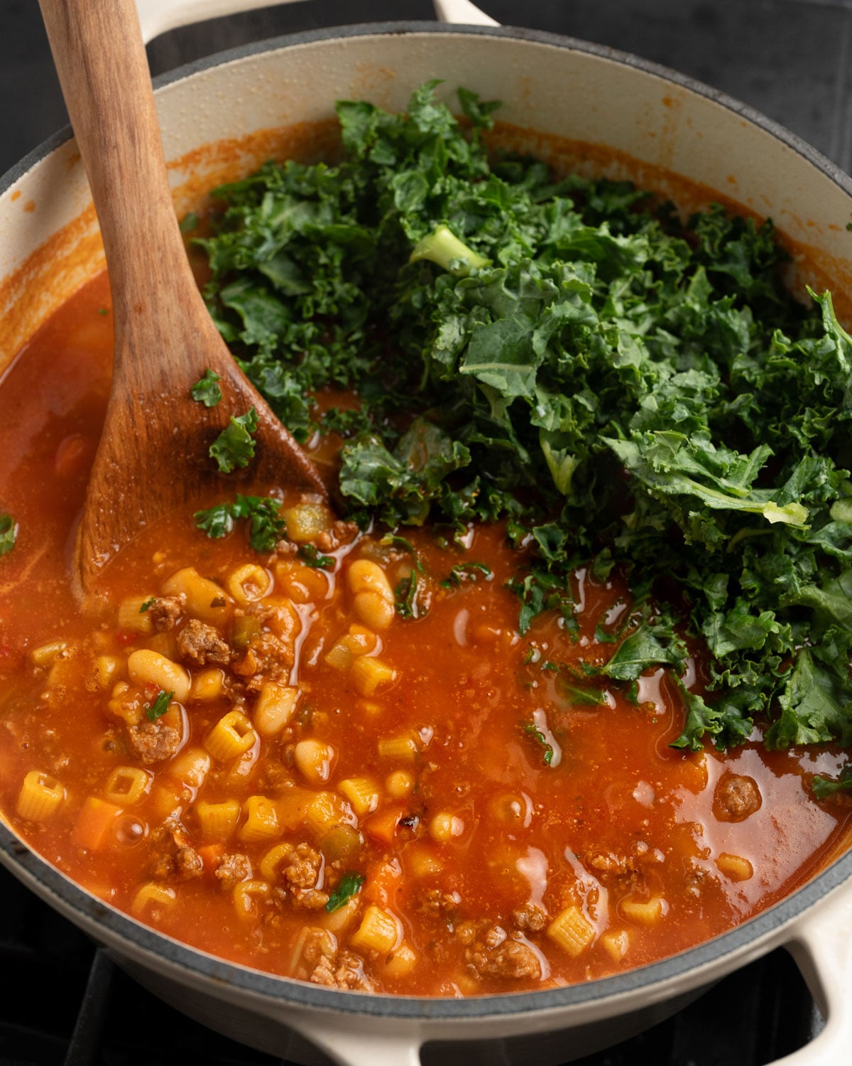 cooked pasta fagioli in a Dutch oven with chopped kale added